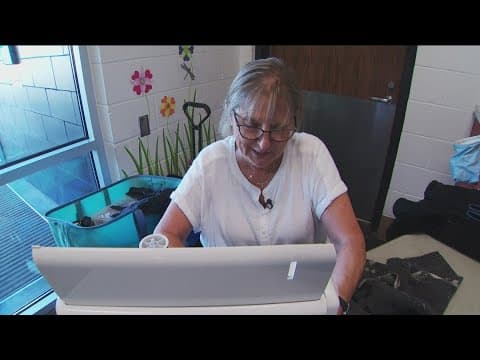 Volunteer seamstress mending clothes of the homeless sits behind her sewing station one last time